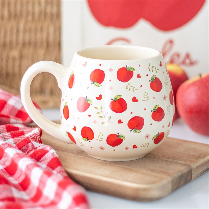 Mug with red apple pattern on a wooden board with apples in the background