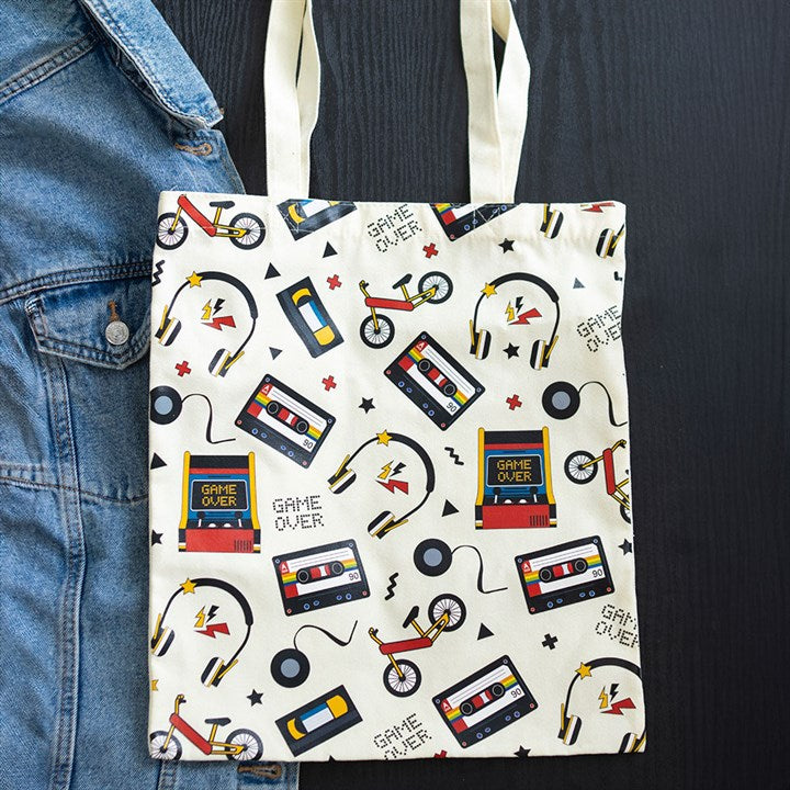 Tote bag with retro design featuring cassette tapes, bicycles, and 'Game Over' signs on a white background.