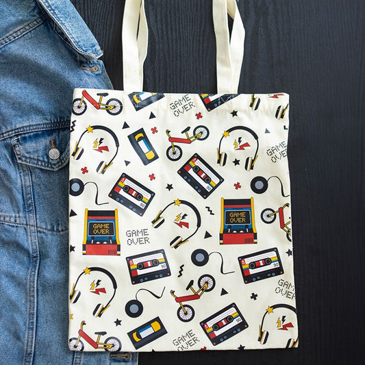 Tote bag with retro design featuring cassette tapes, bicycles, and 'Game Over' signs on a white background.