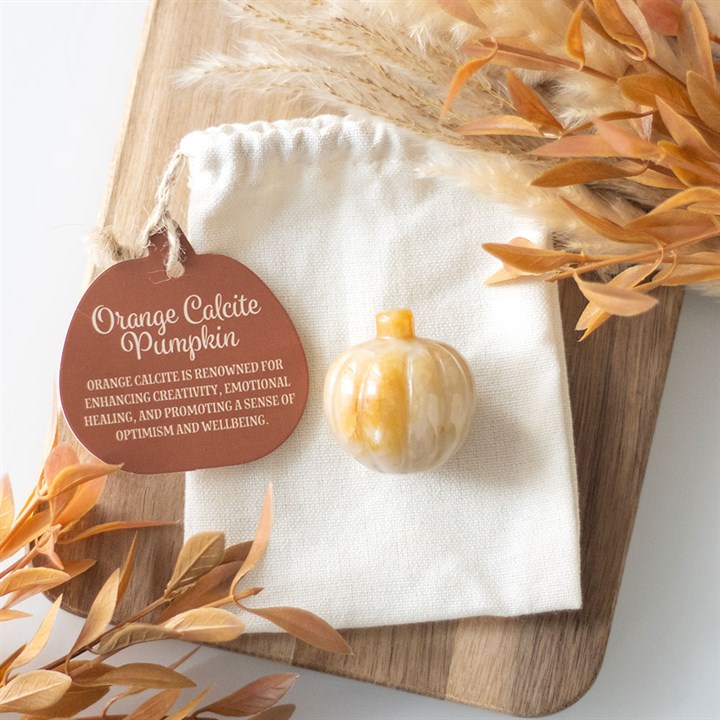 Decorative pumpkin with orange calcite on a white cloth, surrounded by dried leaves.