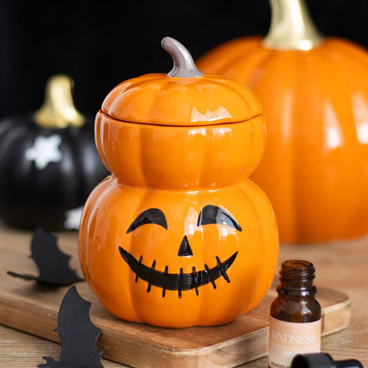 Orange ceramic pumpkin with a face on a wooden surface, surrounded by other pumpkins.