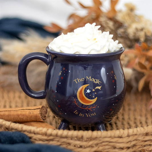 Navy mug with moon and star design, filled with hot chocolate and whipped cream, on a woven surface.