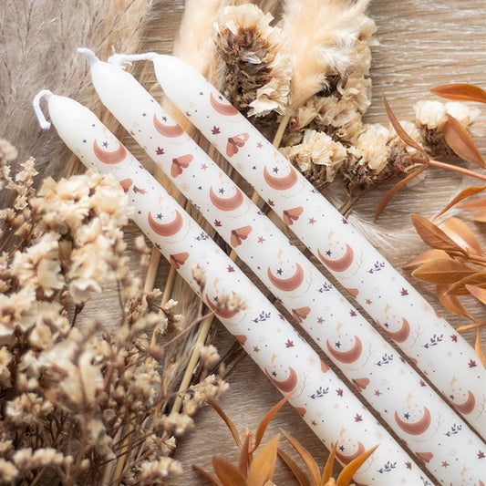 White candles with pink moon and heart patterns on a wooden surface with dried flowers.
