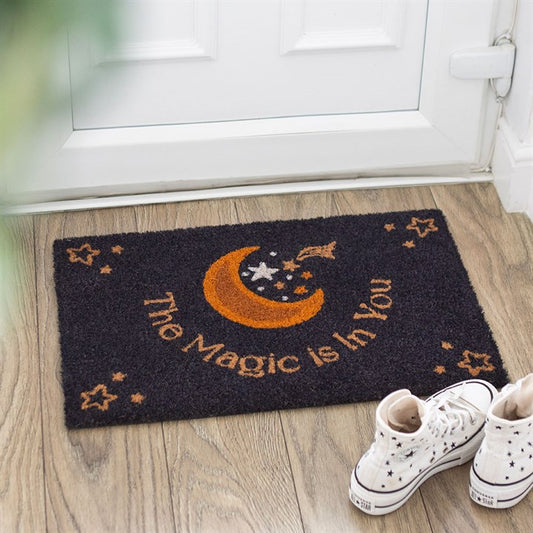 Decorative doormat with 'The Magic is in You' text and moon design on a wooden floor.