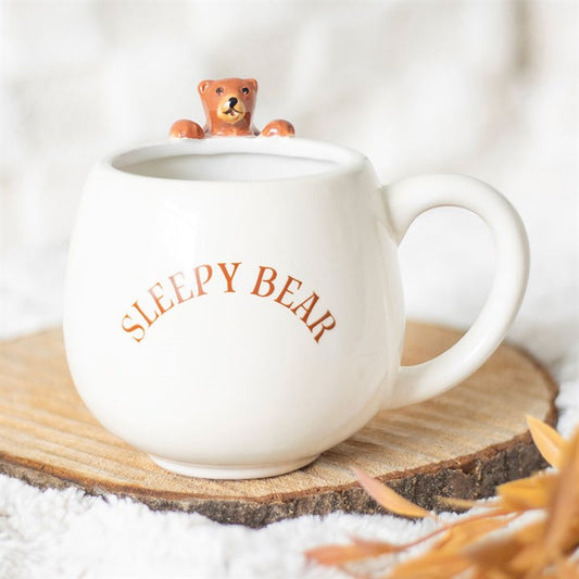 White mug with 'Sleepy Bear' text and a small bear figurine on a wooden coaster.