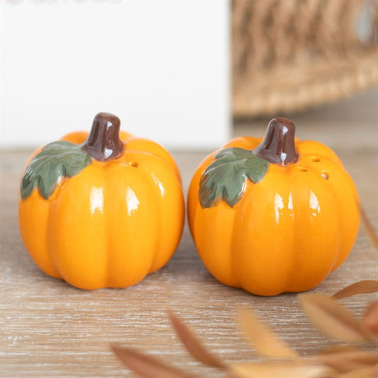 Two ceramic pumpkins with green leaves and brown stems on a wooden surface.