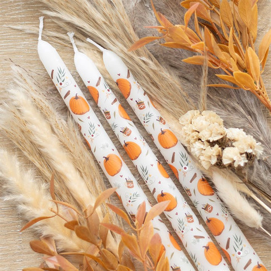 Set of white candles with pumpkin design on a wooden surface with dried plants.