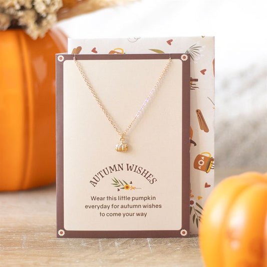 Necklace with 'Autumn Wishes' card on a wooden surface with pumpkins in the background