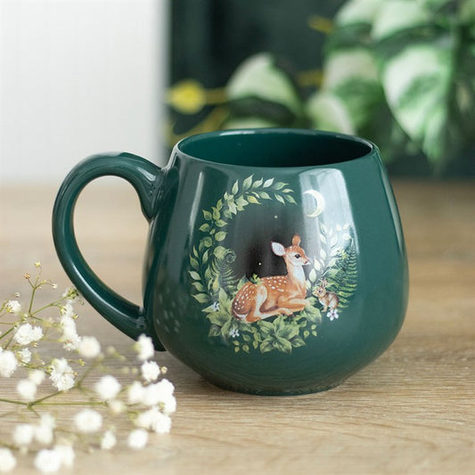 Green mug with deer design on a wooden surface with flowers and plants in the background