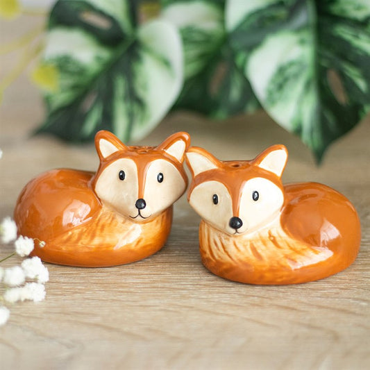Two fox-shaped salt and pepper shakers on a wooden surface with a blurred plant background.
