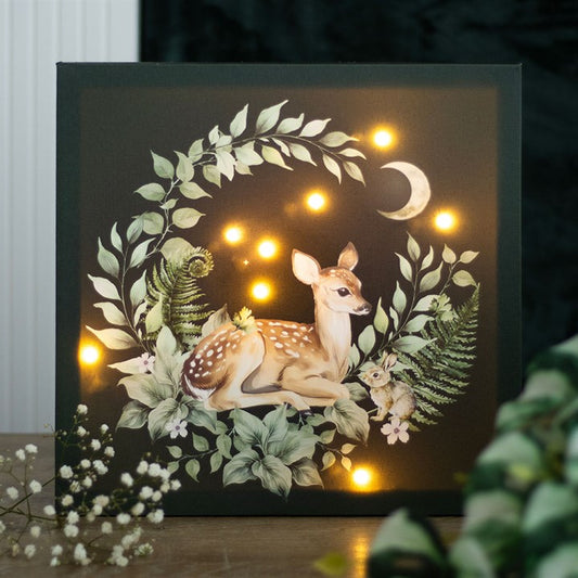Decorative wall art with a deer surrounded by foliage and lights on a dark background